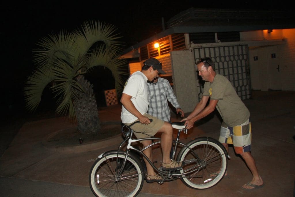 men attempting to ride a bicycle backwards on the beach boardwalk
