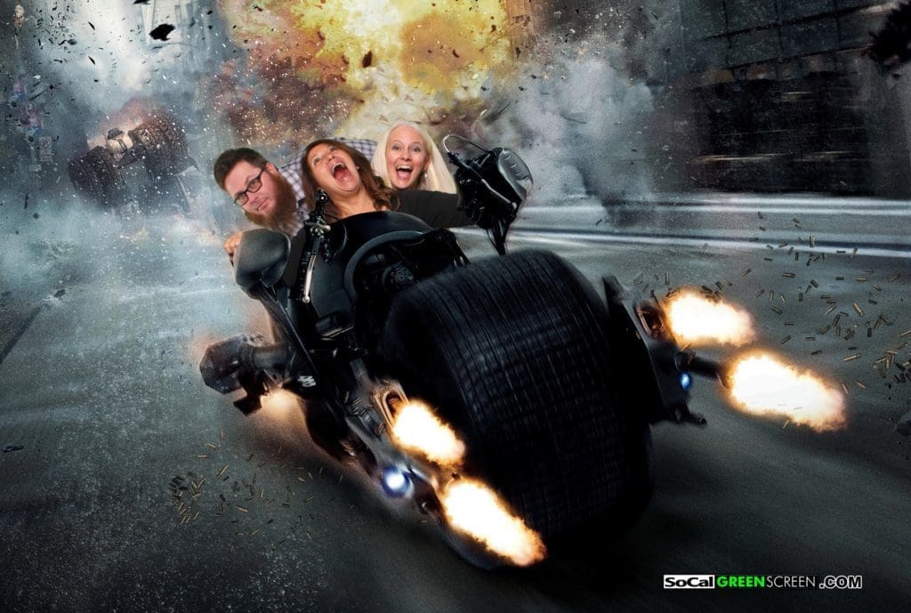 two men and a woman riding Batman's motorcycle away from a menacing monster truck