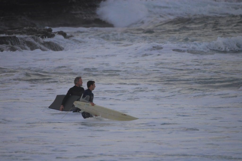 two engineers waist-high in the surf heading out with a boogieboard and surfboard about to shred some waves, dude
